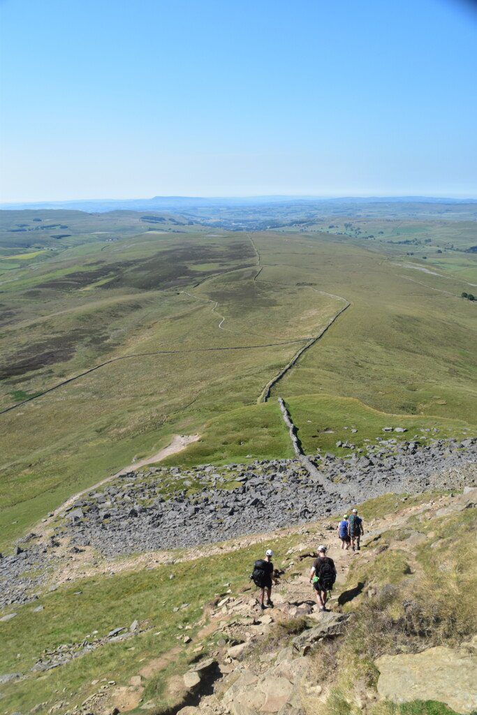 Four trekkers heading down the slopes of Yorkshire's Pen-y-Ghent on a cloudless day