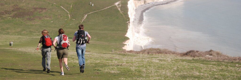 Three hikers on the Seven Sisters at the end of the South Downs Way, jogging downhill away from the camera