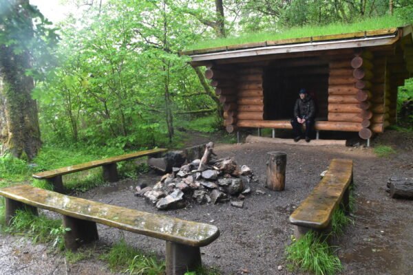 wild campsite on the great glen way with a wooden shelter and fire pit surrounded by benches
